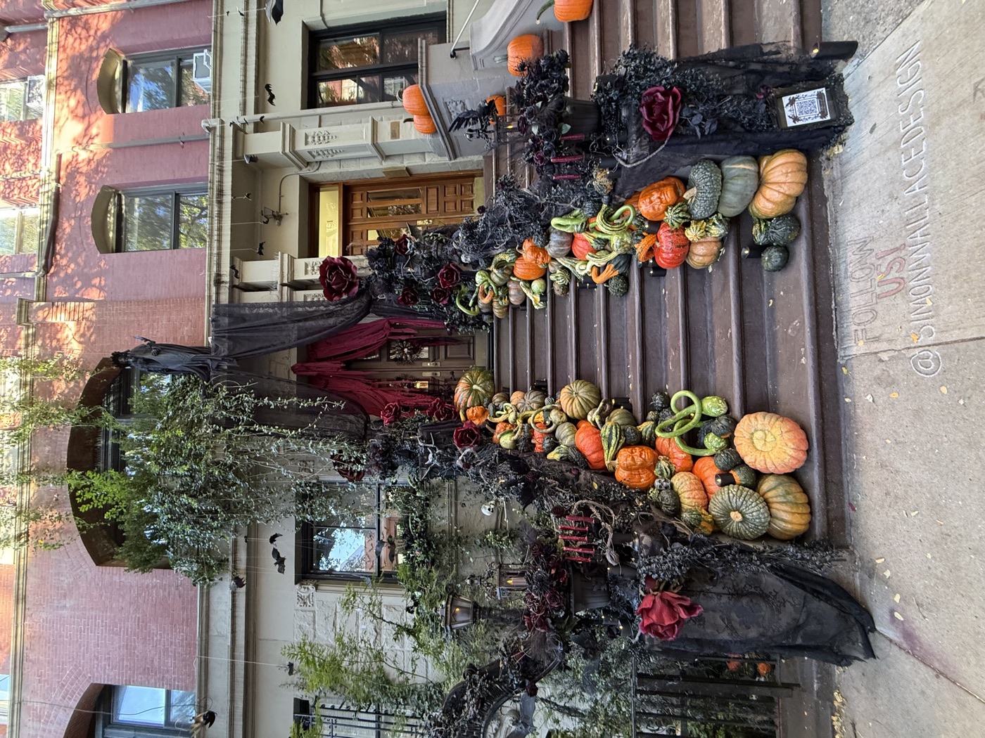Pumpkins and gourds line a brownstone staircase beneath black drapes, roses, and hanging Halloween bats